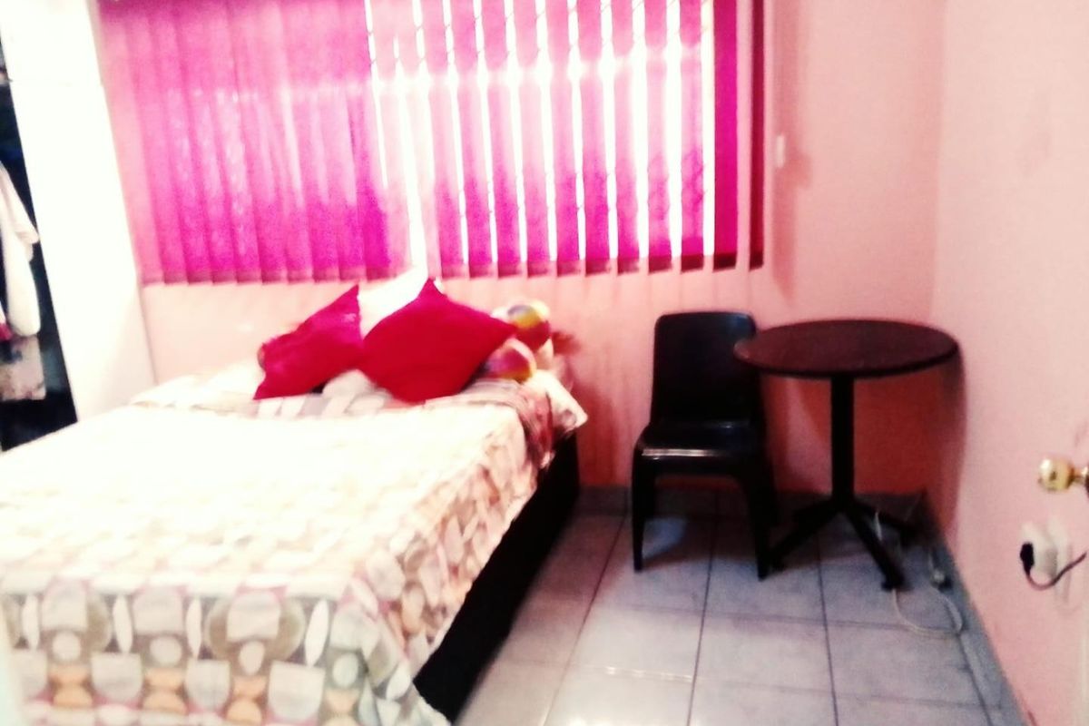 A bedroom featuring tiled flooring and vertical window blinds, currently furnished with a bed and small seating area.