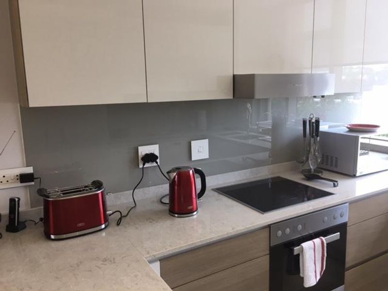 Modern kitchen featuring sleek glossy cabinetry, stone countertops, a glass splashback, and integrated appliances including an induction hob and built-in oven.