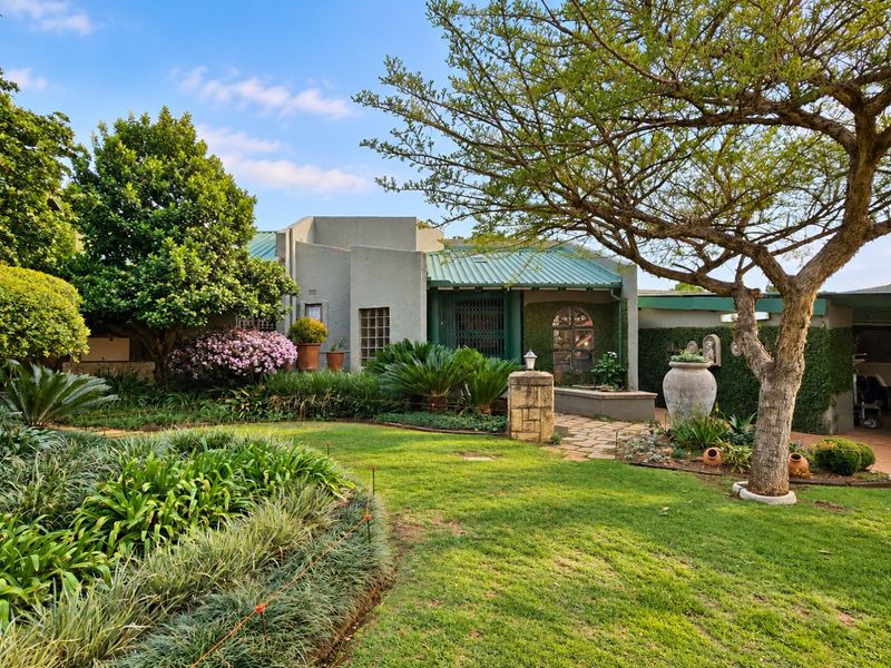 A well-maintained rear garden featuring a lush lawn, mature trees, and a stone pathway leading to the residence with a metal roof.