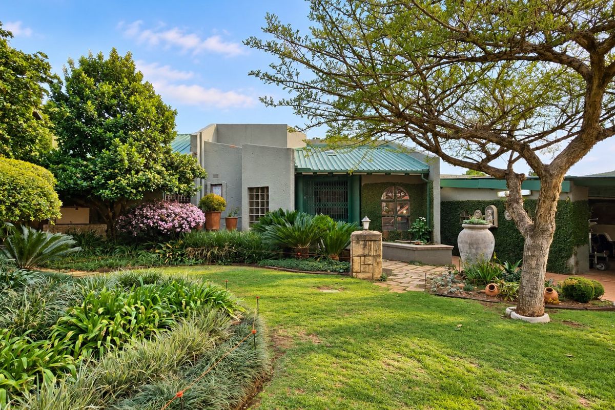 A well-maintained rear garden featuring a lush lawn, mature trees, and a stone pathway leading to the residence with a metal roof.