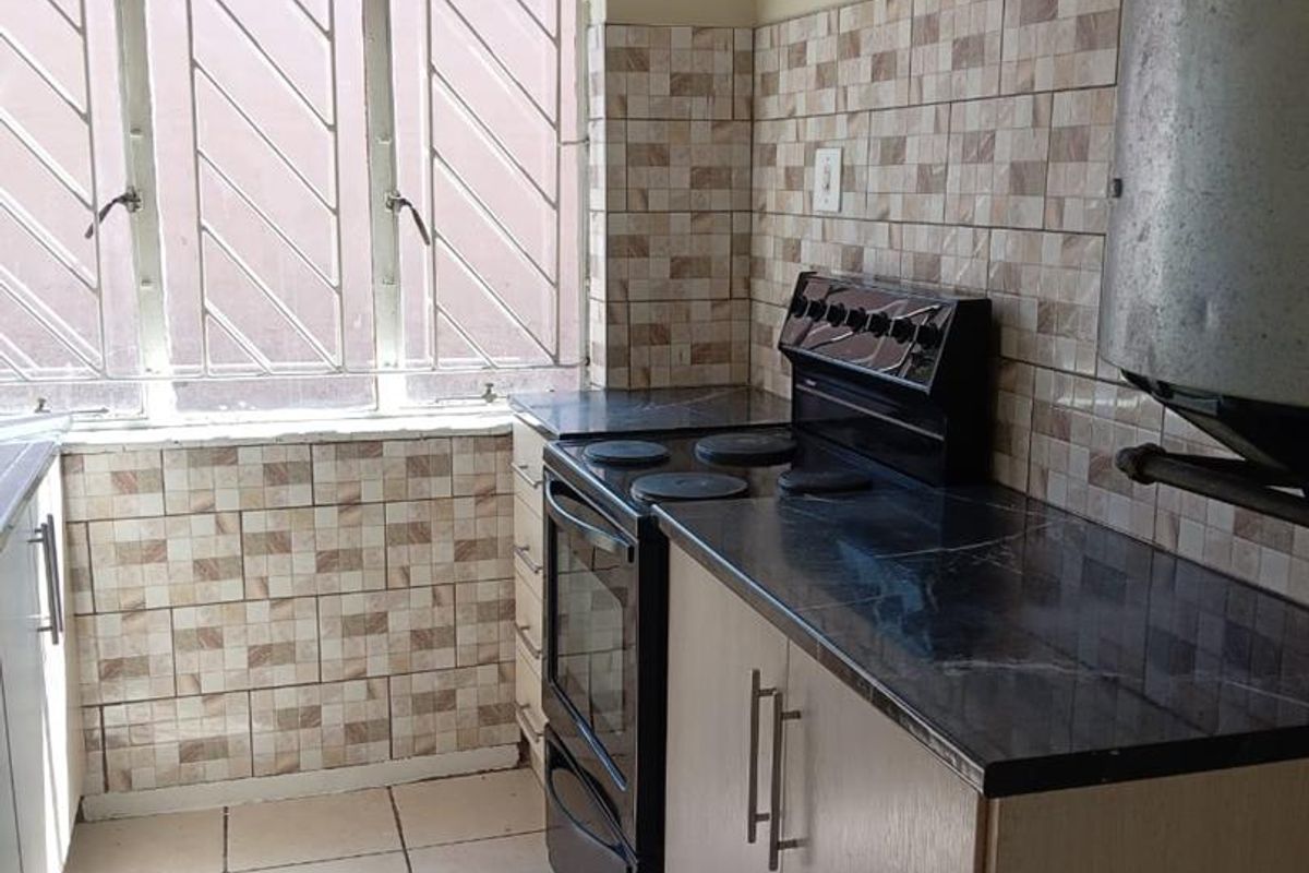 A functional kitchen featuring built-in cabinetry, laminate countertops, a freestanding stove, and tiled finishes, providing a practical workspace with natural light.