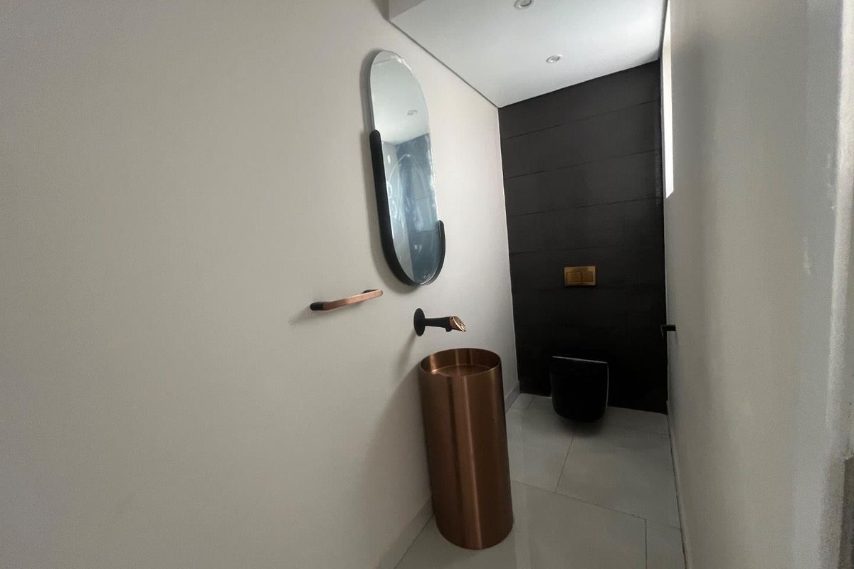 Modern guest bathroom featuring a sleek copper pedestal basin, wall-mounted tap, and a contemporary black wall-hung toilet with dark tiled accent wall.