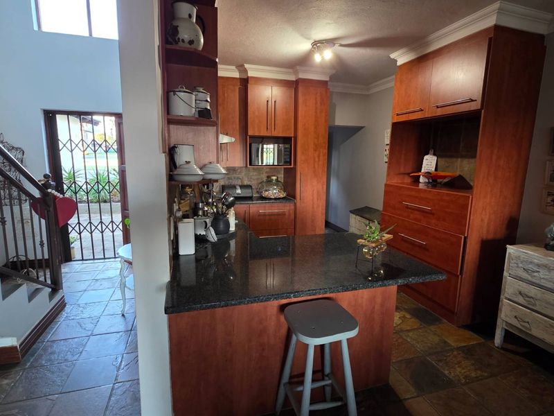 A kitchen featuring warm-toned wooden cabinetry, granite countertops, and a breakfast bar, adjacent to an entryway with a staircase and security gate.