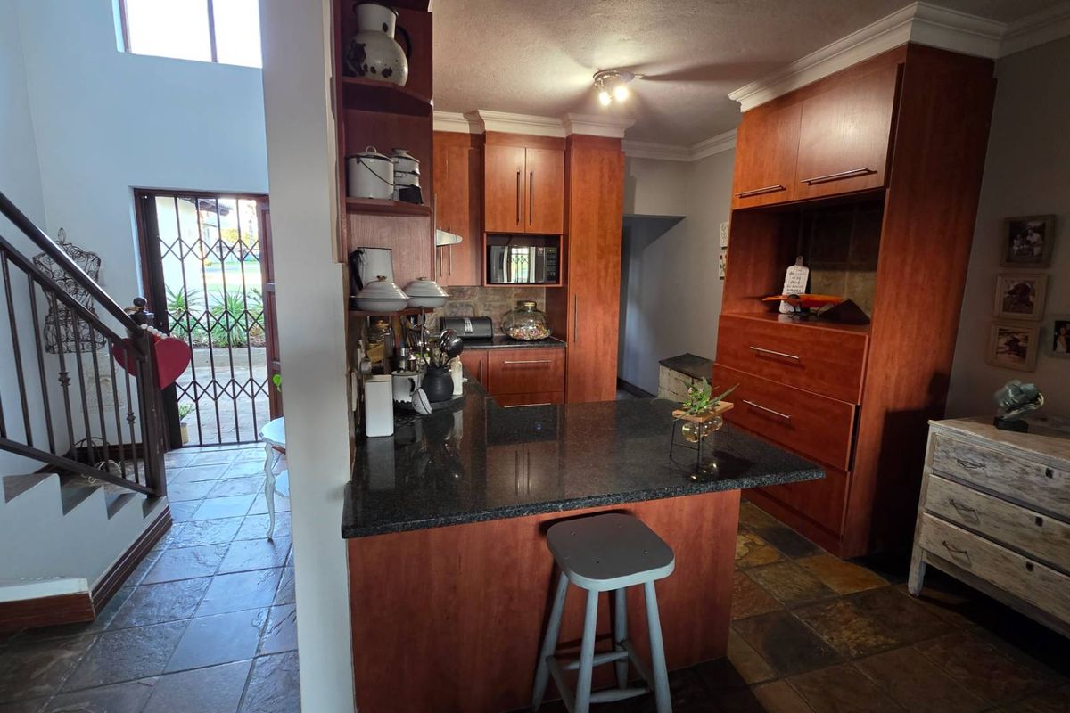 A kitchen featuring warm-toned wooden cabinetry, granite countertops, and a breakfast bar, adjacent to an entryway with a staircase and security gate.