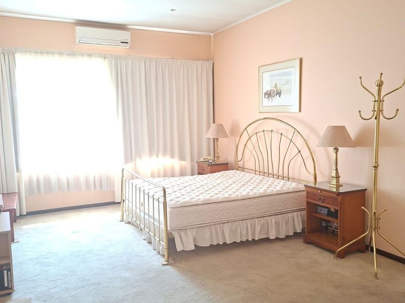 A spacious bedroom featuring neutral carpeting, a wall-mounted split-system air conditioner, and large windows with fitted curtains.