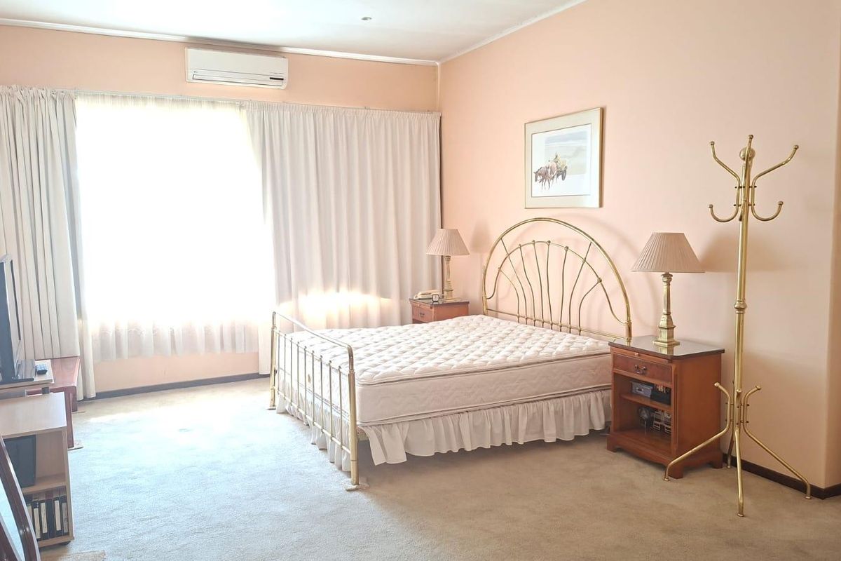 A spacious bedroom featuring neutral carpeting, a wall-mounted split-system air conditioner, and large windows with fitted curtains.
