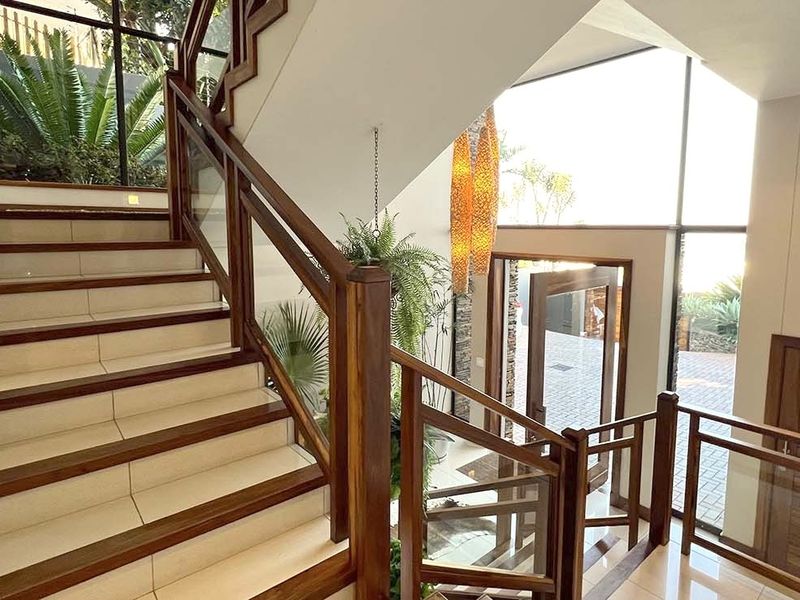 Bright and modern entrance hall featuring a grand staircase with wooden handrails, glass balustrades, and large windows allowing for abundant natural light.