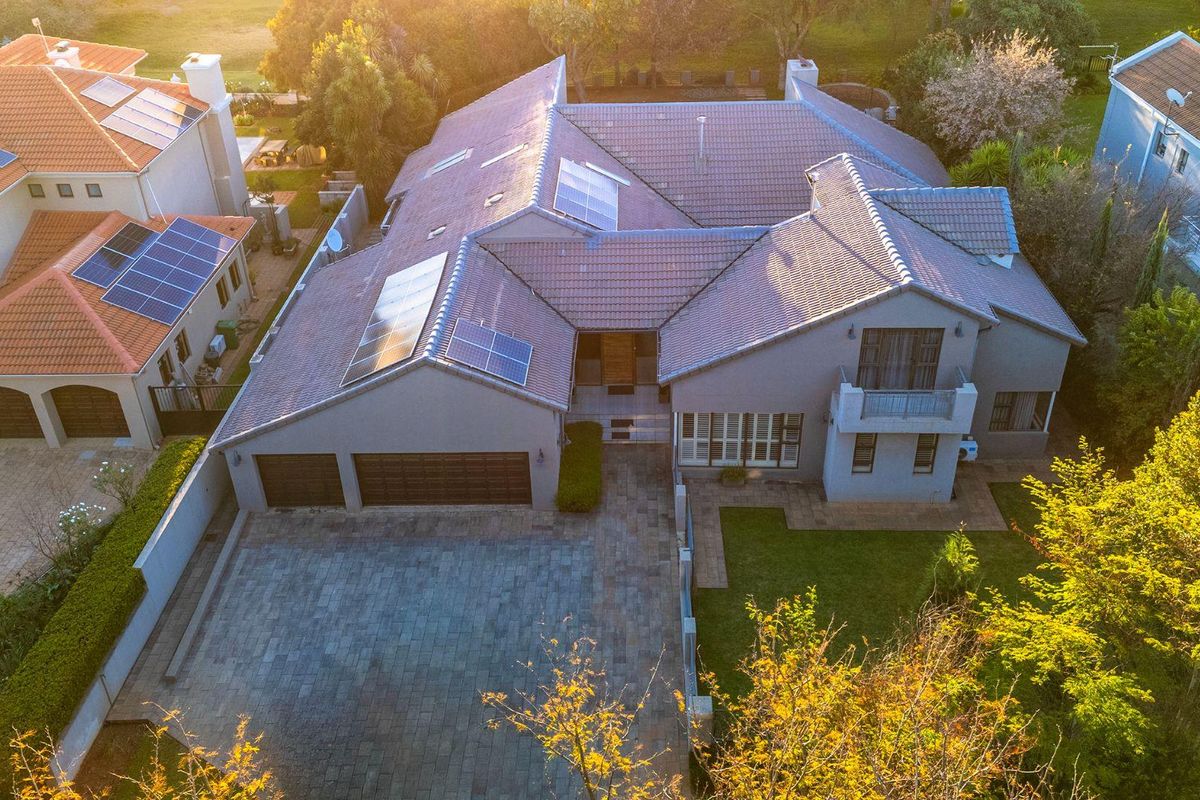 Aerial view of a large residential property featuring a tiled roof, solar panels, paved driveway, double garage, and landscaped garden.