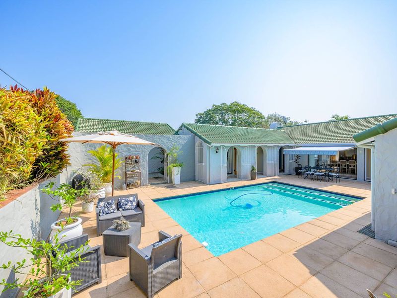 A well-maintained outdoor pool area featuring a tiled deck, arched architectural details, and a green tiled roof, perfect for outdoor relaxation and entertainment.