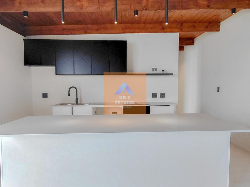 Modern kitchen featuring a central island, sleek black cabinetry, and exposed timber ceiling beams, offering a clean and contemporary aesthetic.