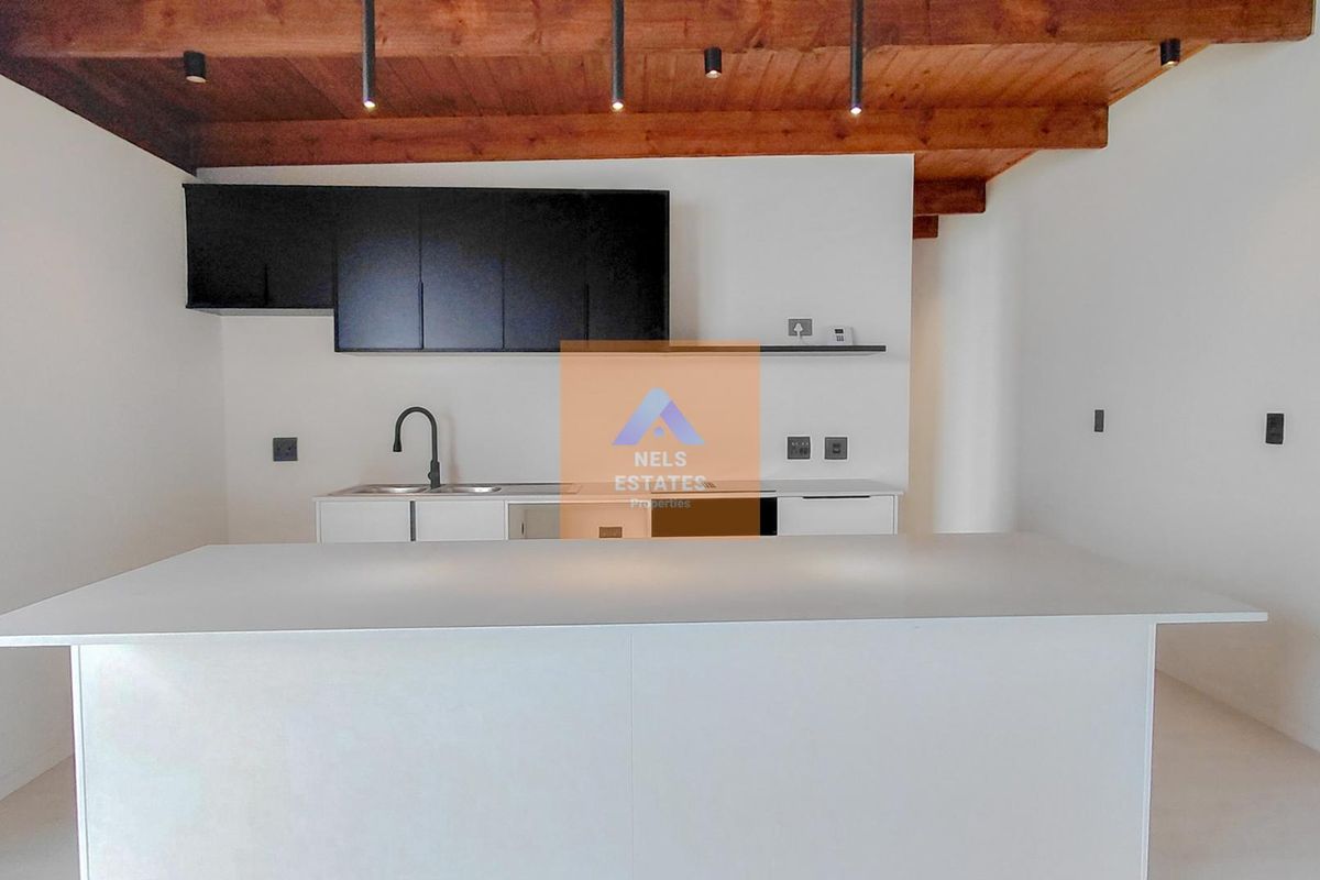 Modern kitchen featuring a central island, sleek black cabinetry, and exposed timber ceiling beams, offering a clean and contemporary aesthetic.