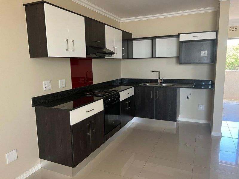 Modern kitchen featuring dark and white cabinetry, granite countertops, built-in oven, hob, extractor fan, and a red glass splashback with tiled flooring.