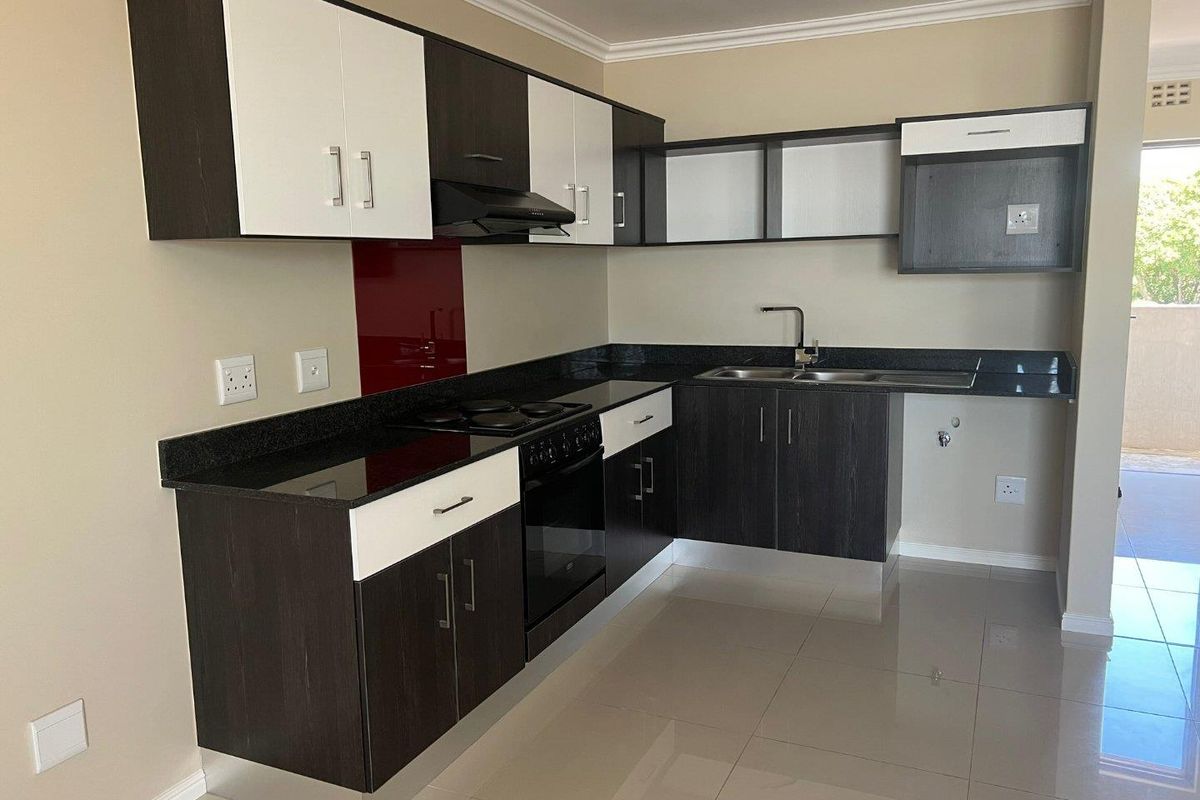 Modern kitchen featuring dark and white cabinetry, granite countertops, built-in oven, hob, extractor fan, and a red glass splashback with tiled flooring.