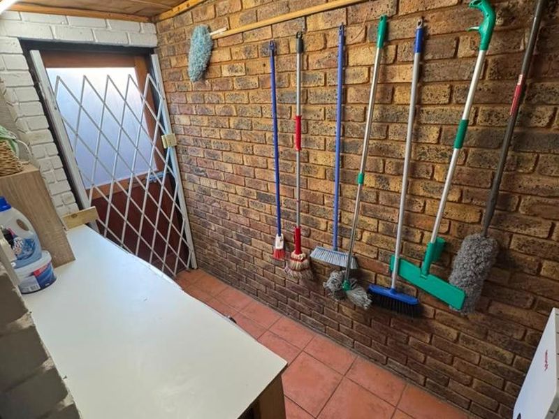 A functional utility or storage area featuring exposed brick walls, tiled flooring, and a security gate, suitable for laundry or general storage purposes.