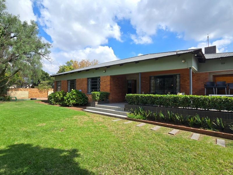 A well-maintained rear exterior view of a brick house featuring a covered patio, established garden, and secure window treatments.