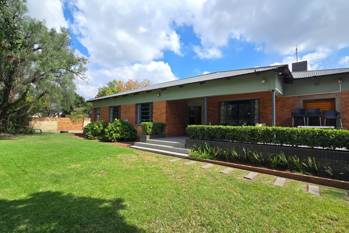 A well-maintained rear exterior view of a brick house featuring a covered patio, established garden, and secure window treatments.