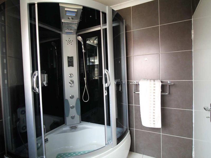 A modern bathroom featuring a corner enclosed shower unit with integrated jets and dark tiled wall finishes.