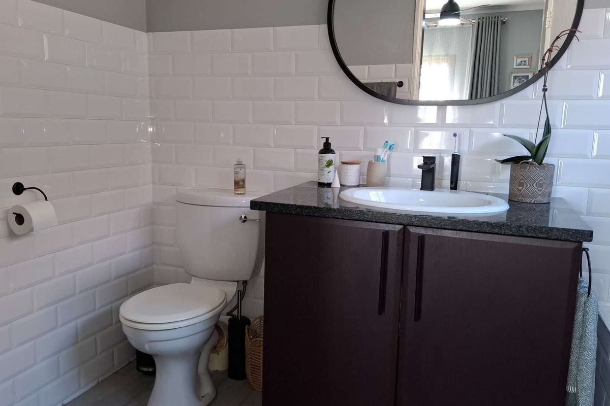 A modern bathroom featuring a dark vanity with a granite countertop, white subway tile wall cladding, and a contemporary round mirror.