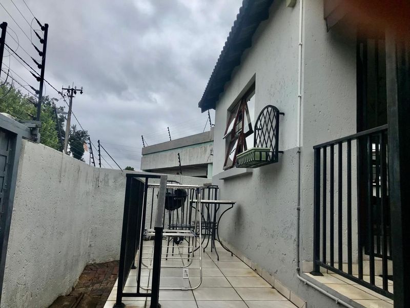 A compact outdoor patio area featuring tiled flooring, metal security railings, and perimeter electric fencing, providing a functional exterior space.