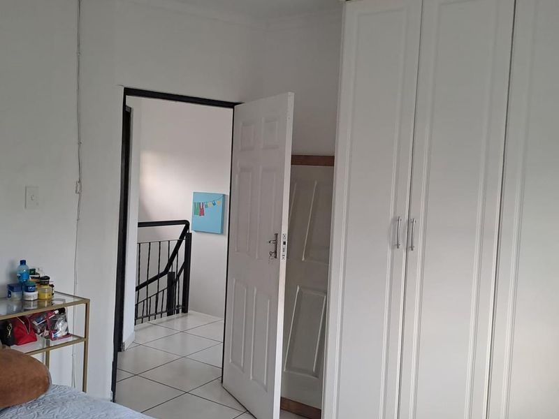 A bedroom featuring white built-in wardrobes and tiled flooring, with an open doorway leading to a staircase landing.