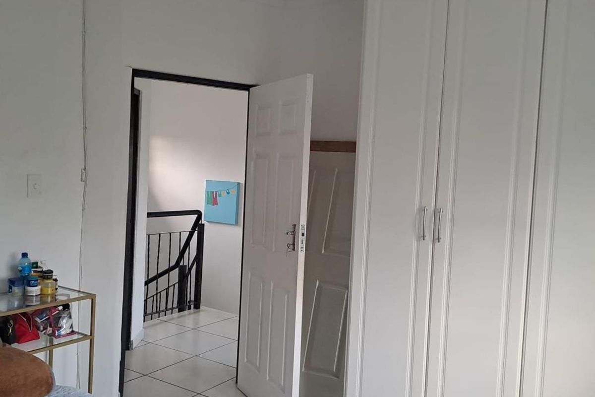 A bedroom featuring white built-in wardrobes and tiled flooring, with an open doorway leading to a staircase landing.