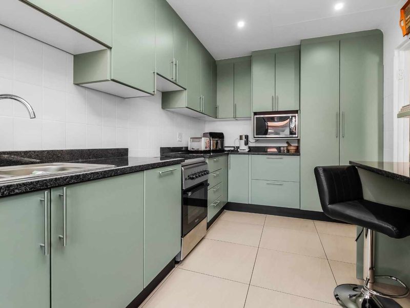 Modern kitchen featuring sage green cabinetry, granite countertops, stainless steel appliances, and tiled flooring with a breakfast bar area.
