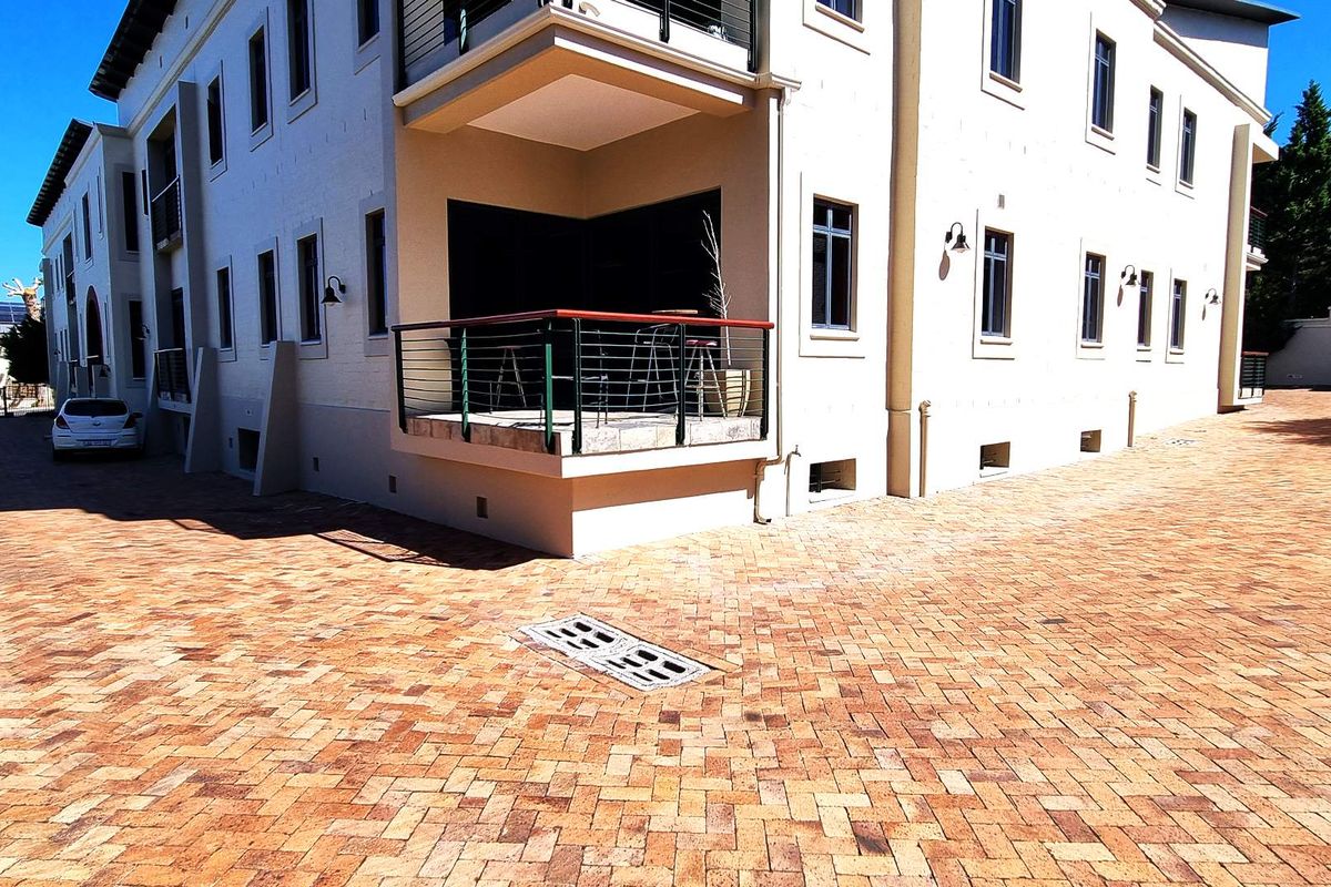 Exterior view of the office building featuring paved driveway, raised patio area with metal railing, and exterior wall-mounted lighting fixtures.