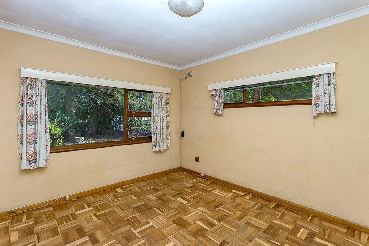 An empty bedroom featuring original parquet flooring, timber window frames with security bars, and neutral wall finishes.