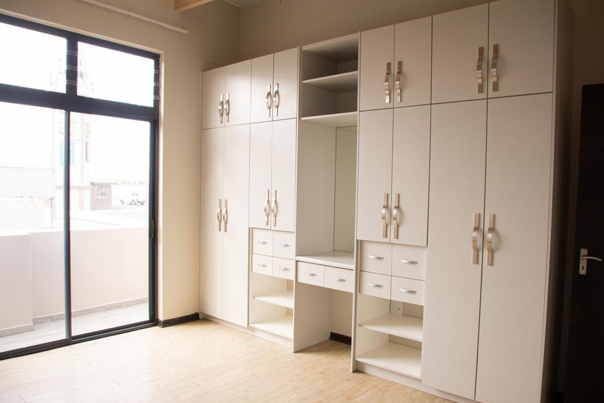 A bright bedroom featuring extensive floor-to-ceiling built-in cabinetry, laminate flooring, and a large sliding glass door providing access to an outdoor area.
