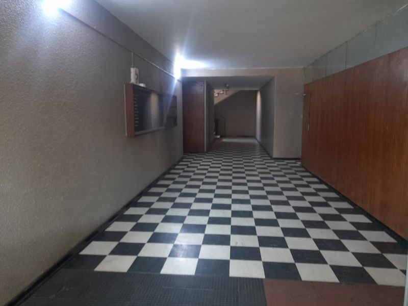 A spacious apartment building hallway featuring classic checkerboard floor tiling and wood paneling, leading towards a staircase.