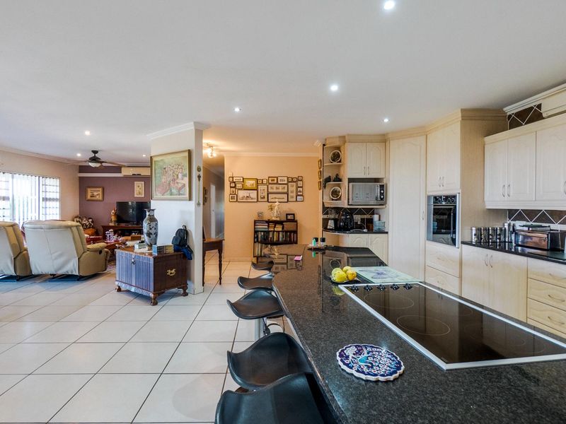 Open-plan living area featuring a kitchen with granite countertops, built-in oven, and induction hob, flowing into a spacious lounge with tiled flooring.