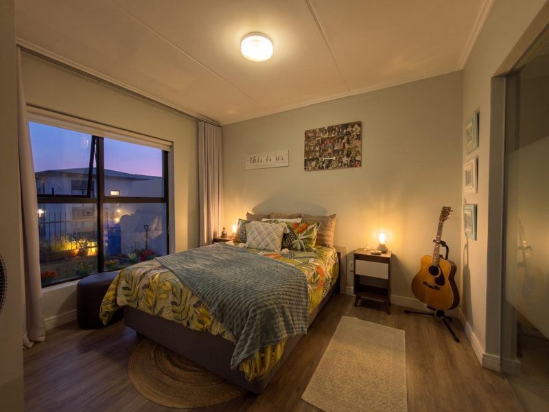 A cozy bedroom featuring laminate flooring, a large window with natural light, and neutral wall tones.