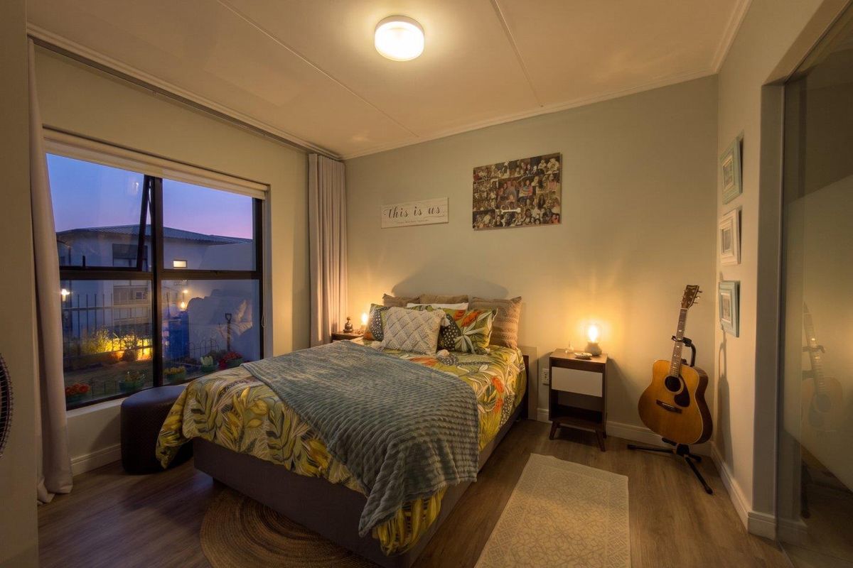 A cozy bedroom featuring laminate flooring, a large window with natural light, and neutral wall tones.