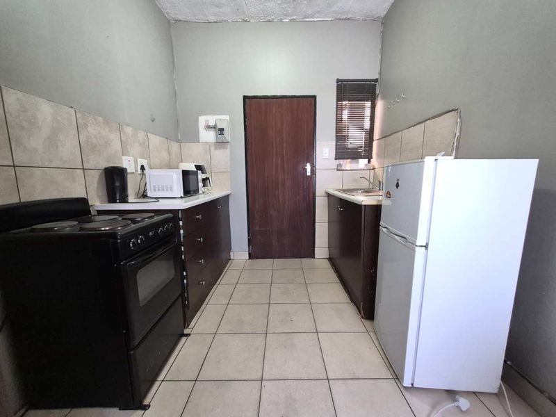 A functional kitchen featuring tiled flooring, a tiled backsplash, built-in cabinetry, and a stainless steel sink, requiring cosmetic updates to improve its overall condition.