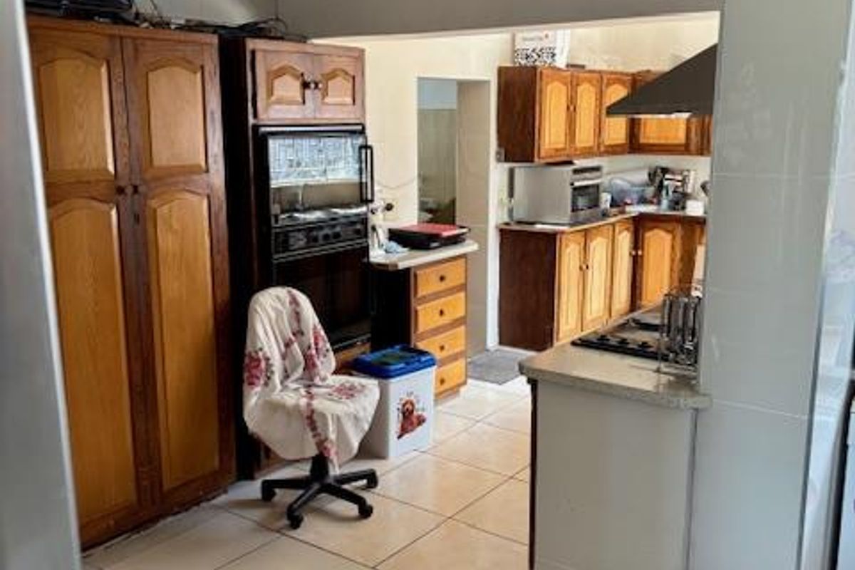 A functional kitchen featuring wooden cabinetry, built-in oven, and tiled flooring, offering a practical layout with potential for modernization.