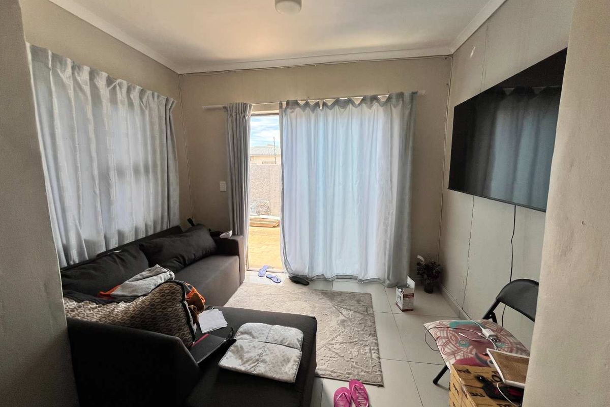 A compact living room featuring tiled flooring, sliding glass doors leading to an outdoor area, and wall-mounted television connectivity.