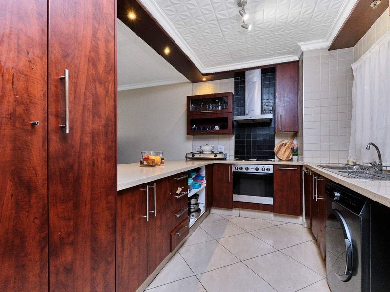 A functional kitchen featuring dark wood cabinetry, stone countertops, a built-in oven with extractor fan, and tiled flooring.