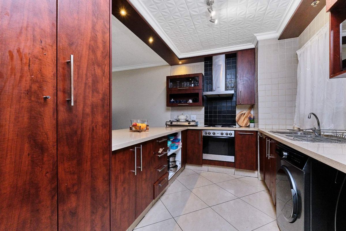 A functional kitchen featuring dark wood cabinetry, stone countertops, a built-in oven with extractor fan, and tiled flooring.