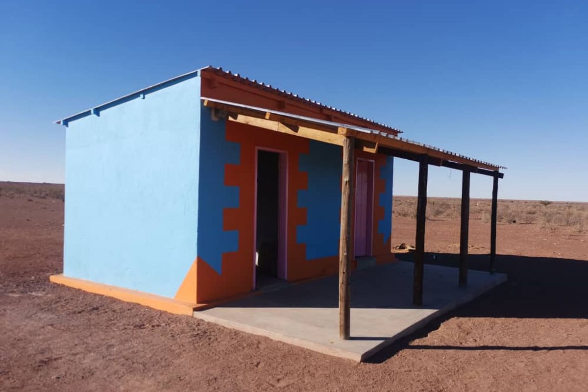 A small, brightly painted outbuilding on a farm, featuring a covered patio area with timber support posts and a corrugated metal roof.
