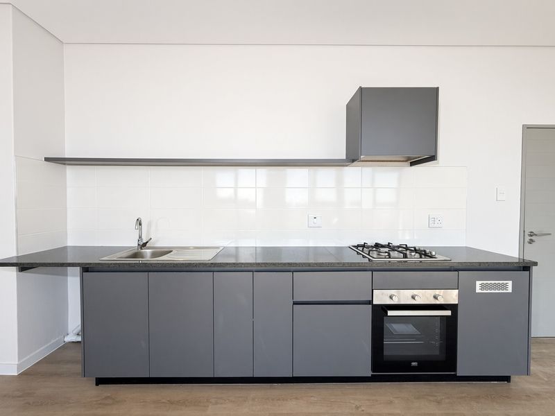 Modern kitchen featuring sleek grey cabinetry, stone countertops, integrated gas hob, built-in oven, and a clean tiled splashback in a minimalist design.