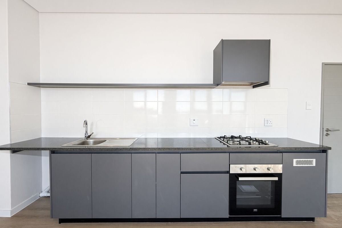 Modern kitchen featuring sleek grey cabinetry, stone countertops, integrated gas hob, built-in oven, and a clean tiled splashback in a minimalist design.