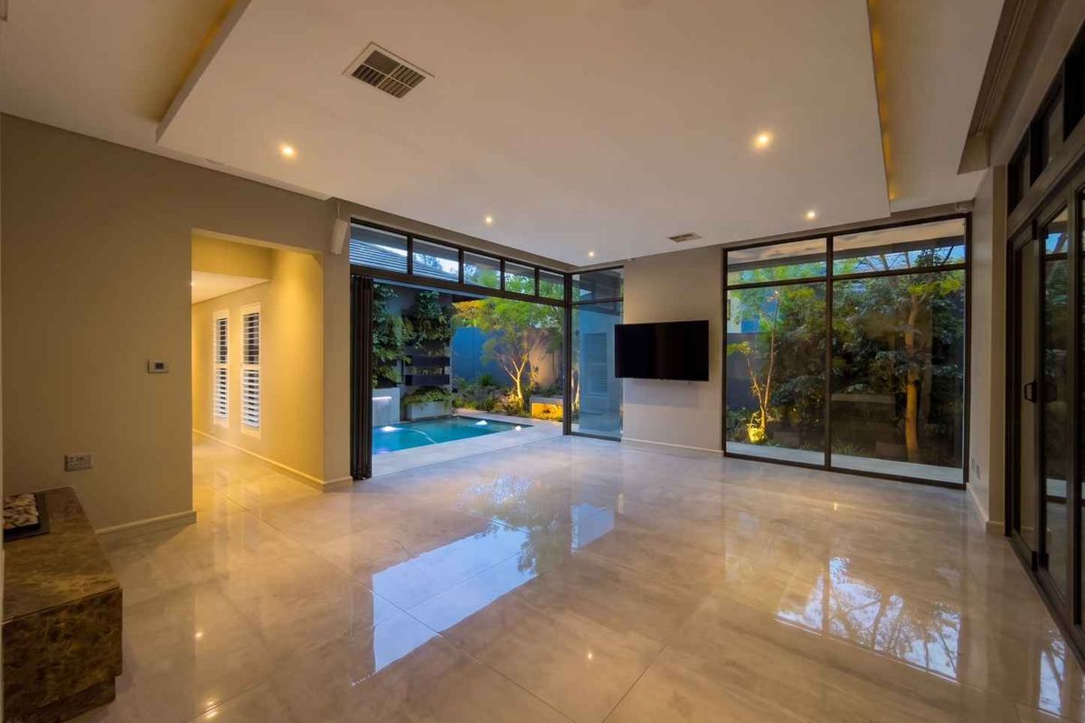 Spacious modern living area featuring large format polished floor tiles, recessed ceiling lighting, and expansive glass sliding doors opening onto a private pool courtyard.