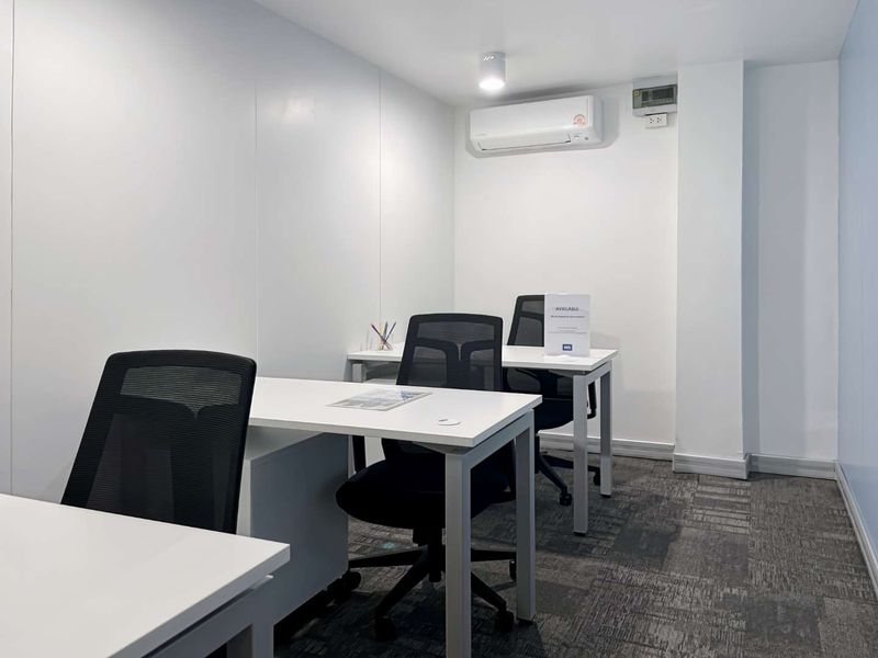 A clean, functional office space featuring carpeted flooring, a wall-mounted air conditioning unit, and modern recessed lighting.
