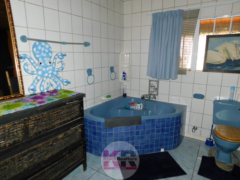 A dated bathroom featuring a blue corner bathtub, matching toilet, and white wall tiling. The space would benefit from modern updates to finishes.