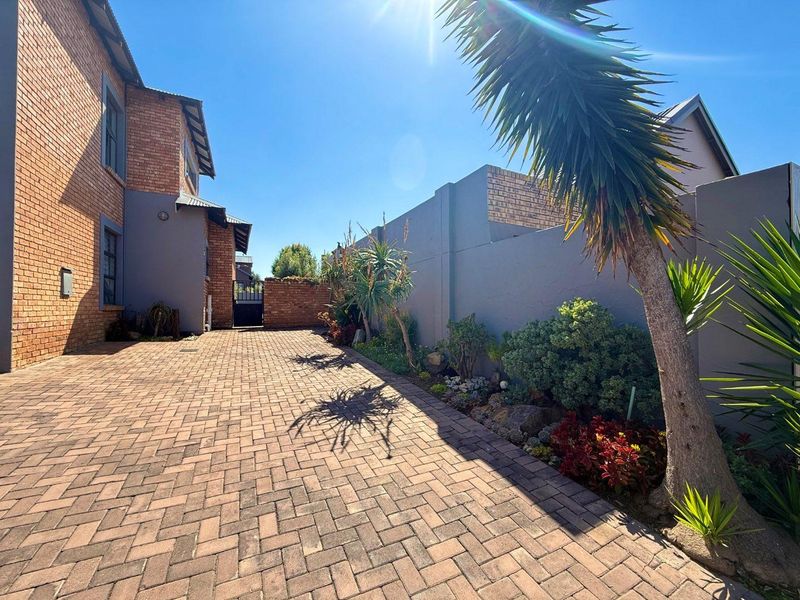 A well-maintained brick-paved driveway leading to a secure gated entrance, featuring a solid boundary wall and established garden landscaping.