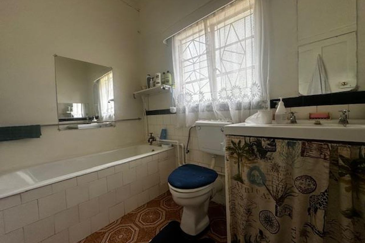 A dated bathroom featuring a standard bathtub, toilet, and vanity basin with original tiling and window security bars.