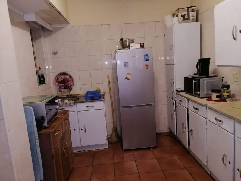 A compact kitchen featuring dated cabinetry, tiled splashbacks, and tiled flooring, offering potential for modernization and improved layout efficiency.