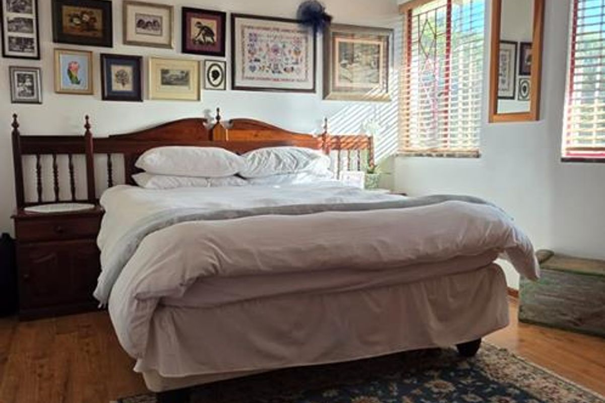 A well-lit bedroom featuring laminate flooring, timber-framed windows with venetian blinds, and a decorative ceiling pendant light.