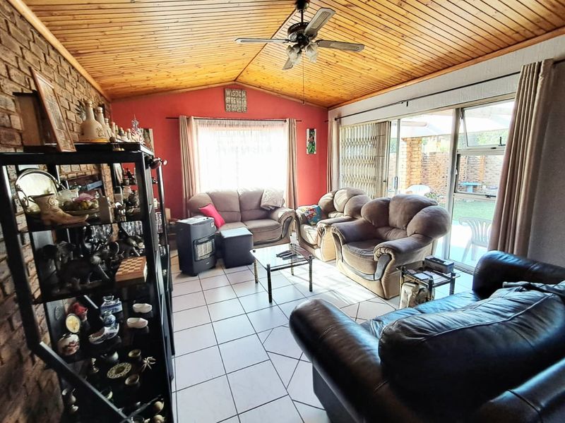 Spacious living room featuring an exposed timber vaulted ceiling, tiled flooring, and large sliding glass doors providing access to the rear patio.