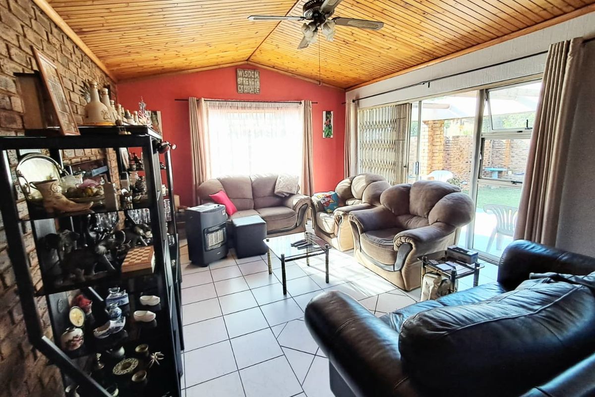 Spacious living room featuring an exposed timber vaulted ceiling, tiled flooring, and large sliding glass doors providing access to the rear patio.